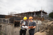 © skarie - Team of construction workers discussing project details with blueprint in construction site.