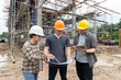 © skarie - Team of construction workers discussing project details with blueprint in construction site.