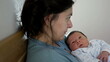 © Marco - Woman holding her newborn baby in a cozy bedroom, working on a laptop, showcasing the blend of parenting and remote work, modern family life, and nurturing maternal care