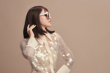 Wall Mural - Woman in white shirt, sunglasses, beige background, hand on ear, posing sideways, looking off to the side