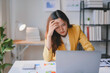 © amnaj - Young business woman feeling tired and having a headache while working on a laptop computer in the office