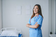 © amnaj - Young female doctor is smiling while standing in a hospital room with her arms folded
