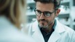 ©  Jovaduplex - A man with glasses intensely focused in conversation with another person, in a professional laboratory setting, highlighting teamwork and concentration with blurred background.