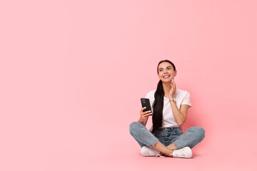 Wall Mural - Smiling woman with smartphone on pink background. Space for text