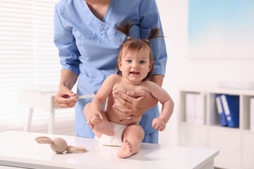 Canvas Print - Pediatrician examining cute little girl with thermometer in clinic, closeup. Checking baby's health