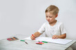 © Валентина Хруслова - A toddler draws with colored pencils in a sketchbook while sitting at a table in the nursery.