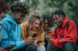 © Anna - Group of smiling diverse teenagers in colorful hoodies laughing and looking at smartphones outdoors. Concepts of friendship, technology, and youthful joy in a natural setting.