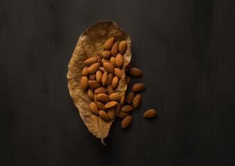 Cleaned almond seeds on a dry almond tree leaf. Artistic food photography of Almonds on black background.