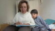 © Marco - Elderly grandmother and young boy sharing a close moment while reading a book on a bed, illustrating warmth, education, and family bonding in a comfortable and loving environment