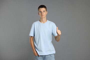 Canvas Print - Teenage boy wearing light blue t-shirt and showing thumbs up on grey background