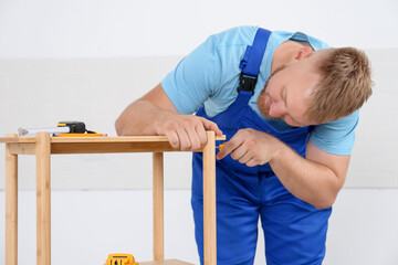 Worker with screwdriver assembling wooden furniture indoors