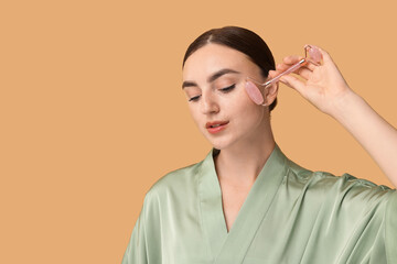 Poster - Beautiful young woman doing facial massage with roller on beige background, space for text