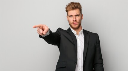 A well-groomed man in a black suit points assertively, showcasing confidence and professionalism against a plain backdrop in a studio setting