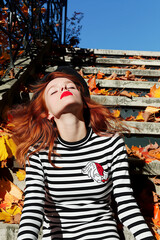 A woman with red hair is wearing a black and white striped shirt and a black hat