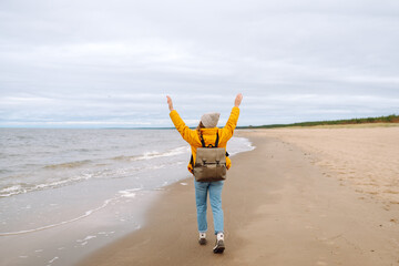 Wall Mural - Back view of  woman tourist walking beach on cloudy day. Cold weather. Calmness and tranquility. Travel, tourism concept.