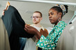© pressmaster - Young African American female tailor and her male colleague looking at unfinished black blazer on hanger while standing by rack