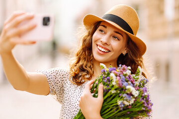 Selfie time. Young woman with a bouquet of wild flowers posing on the street. Blogging concept. Fashion style.