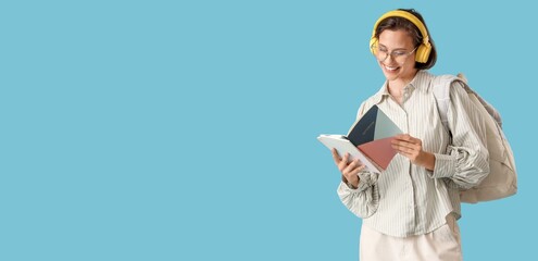 Wall Mural - Happy female student with backpack, headphones and notebooks on blue background with space for text