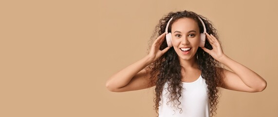 Wall Mural - Happy young African-American woman in headphones on beige background with space for text