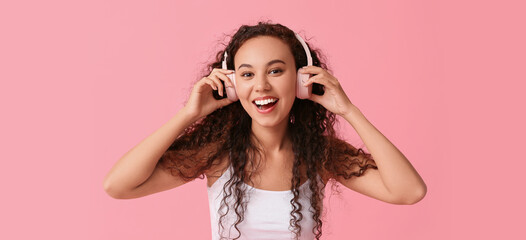 Wall Mural - Happy young African-American woman in headphones on pink background