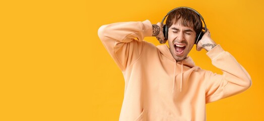 Sticker - Young tattooed man with headphones singing against yellow background with space for text