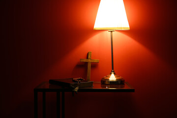 Wall Mural - Holy Bible with prayer beads and lamp on table near red wall