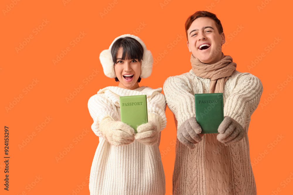 Beautiful young happy couple with passports on orange background. Winter vacation concept