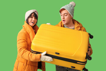 Wall Mural - Beautiful young couple with suitcase on green background. Winter vacation concept