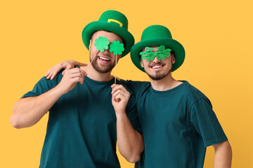 Wall Mural - Funny young men in leprechaun's hats with clovers on yellow background. St. Patrick's Day celebration