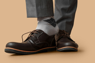 Wall Mural - Legs of young man in elegant shoes on brown background