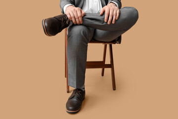 Wall Mural - Young man in elegant shoes sitting on chair against brown background