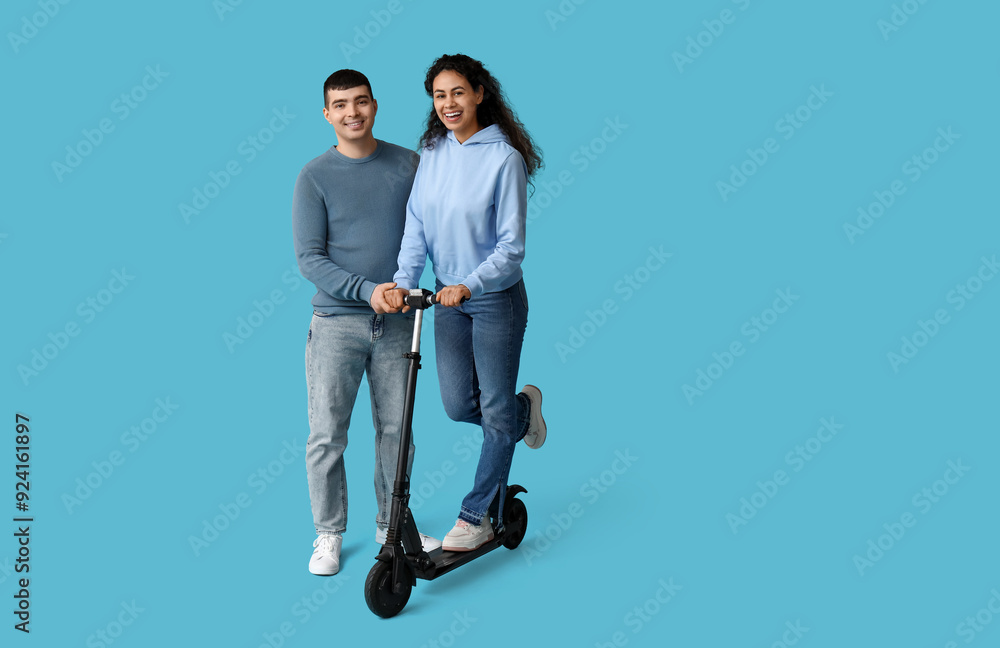 Happy young couple with modern electric kick scooter on blue background