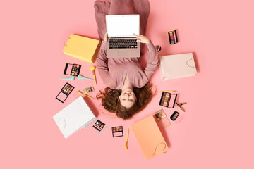 Wall Mural - Beautiful young woman with modern laptop, eyeshadows palettes, makeup brushes and shopping bags on pink background