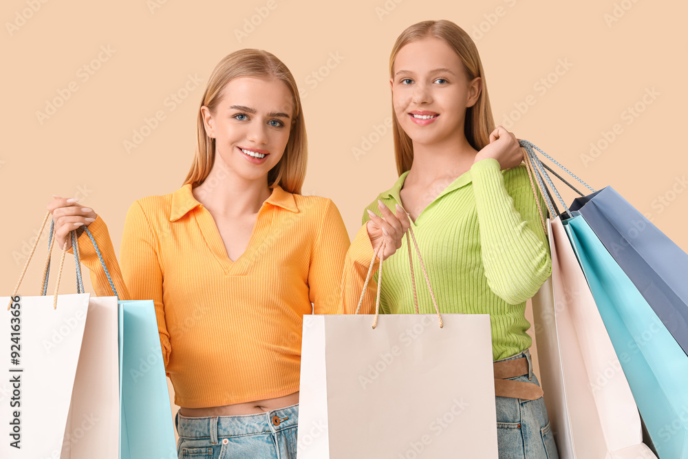 Beautiful young sisters with shopping bags on beige background