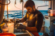 © VisualProduction - A marine biologist, a South Asian man in a wetsuit, analyzes water samples on a research vessel, bathed in the golden glow of the setting sun.