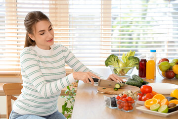 Canvas Print - Young woman cutting cucumber in kitchen. Diet concept