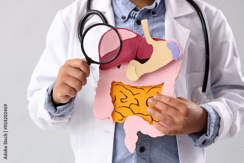 Little doctor with paper digestive system and magnifier on light background, closeup