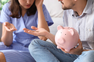 Poster - Young couple sitting on floor with piggy bank and arguing at home. Bankruptcy concept