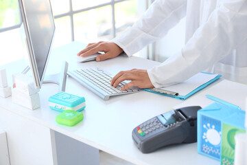 Male pharmacist working with computer at pharmacy, closeup