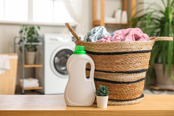 Wall Mural - Wicker basket with laundry, houseplant and bottle of detergent on wooden table in room