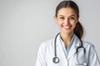 © Ayrum.Design - A smiling young female doctor in a white coat with a stethoscope around her neck stands against a light gray background with ample copyspace, conveying professionalism and approachability