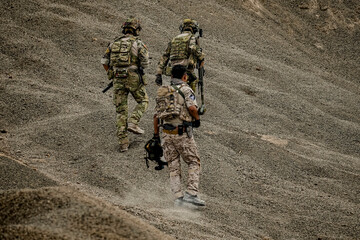 A group of military men in combat gear patrol in the middle of a desert and tropical jungle. Soldiers in full combat gear in dry weather conditions assemble and march on a mission.