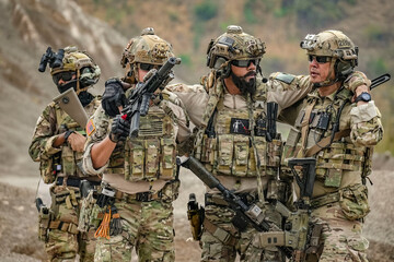 A group of military men in combat gear patrol in the middle of a desert and tropical jungle. Soldiers in full combat gear in dry weather conditions assemble and march on a mission.