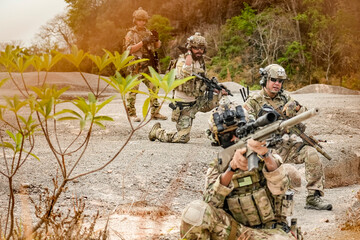 A group of military men in combat gear patrol in the middle of a desert and tropical jungle. Soldiers in full combat gear in dry weather conditions assemble and march on a mission.