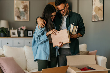 Loving mid aged couple holding and taking out books, unpacking during relocation into a new house.