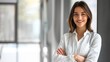 © JINGWEN - Confident businesswoman with crossed arms smiling in modern office, facing camera, embodying success in professional attire with sleek hairstyle.