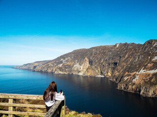 Wall Mural - Young teenager girl explore beautiful nature scenes of Sliabh Liag viewing platform. Famous landmark in Ireland. Warm sunny day. Irish nature landscape. Travel and tourism industry.