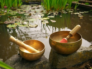 Two singing bowls on rocks with a pond and water lilies in the background