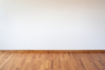 Empty apartment room with white wall and wooden parquet flooring, no people