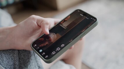 close up of teenager scrolling and watching various video content using mobile phone while sitting o